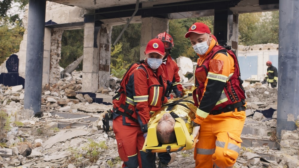 Paramedics Carrying An Injured Person Away From A Destroyed Building On A Stretcher 