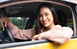 A photo of a woman sitting in her car smiling.