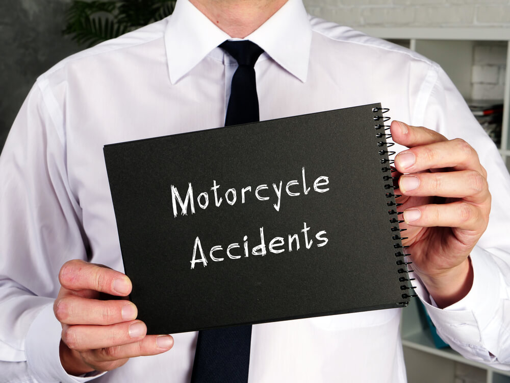 A photo of a man holding up a sign reading "Motorcycle Accidents"